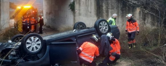 Una dotación de bomberos tuvo que intervenir para excarcelar al conductor del coche, que quedó volcado tras la caída // CPB de Málaga